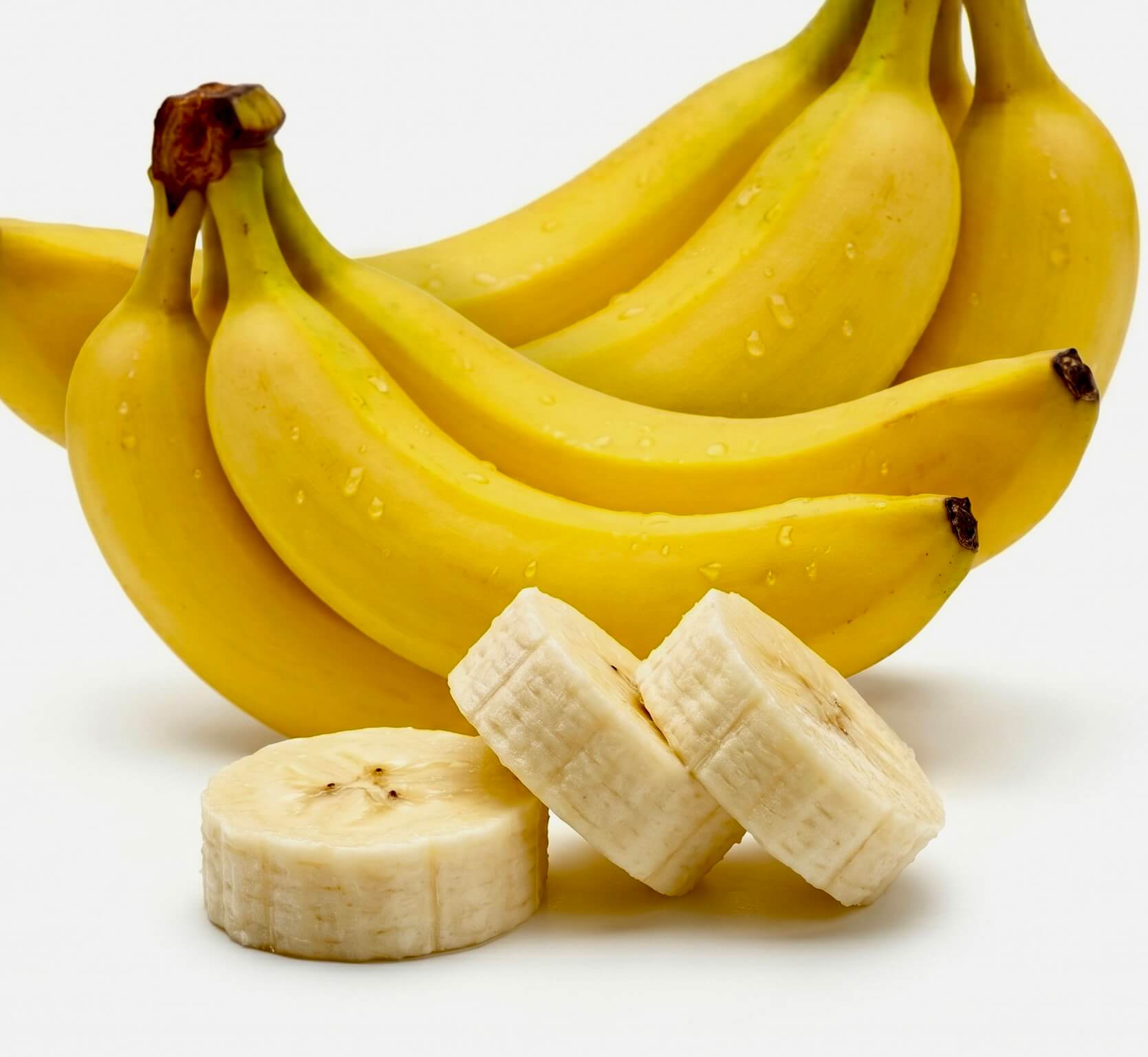 Nahaufnahme einer Staude gelber Bananen mit drei aufgeschnittenen Bananenscheiben im Vordergrund und dem eingeblendeten Text 'Vitamin B6'. Das Bild visualisiert eine natürliche Quelle für diesen Inhaltsstoff der Riddys Premium-Nahrungsergänzung für Hund und Katze.